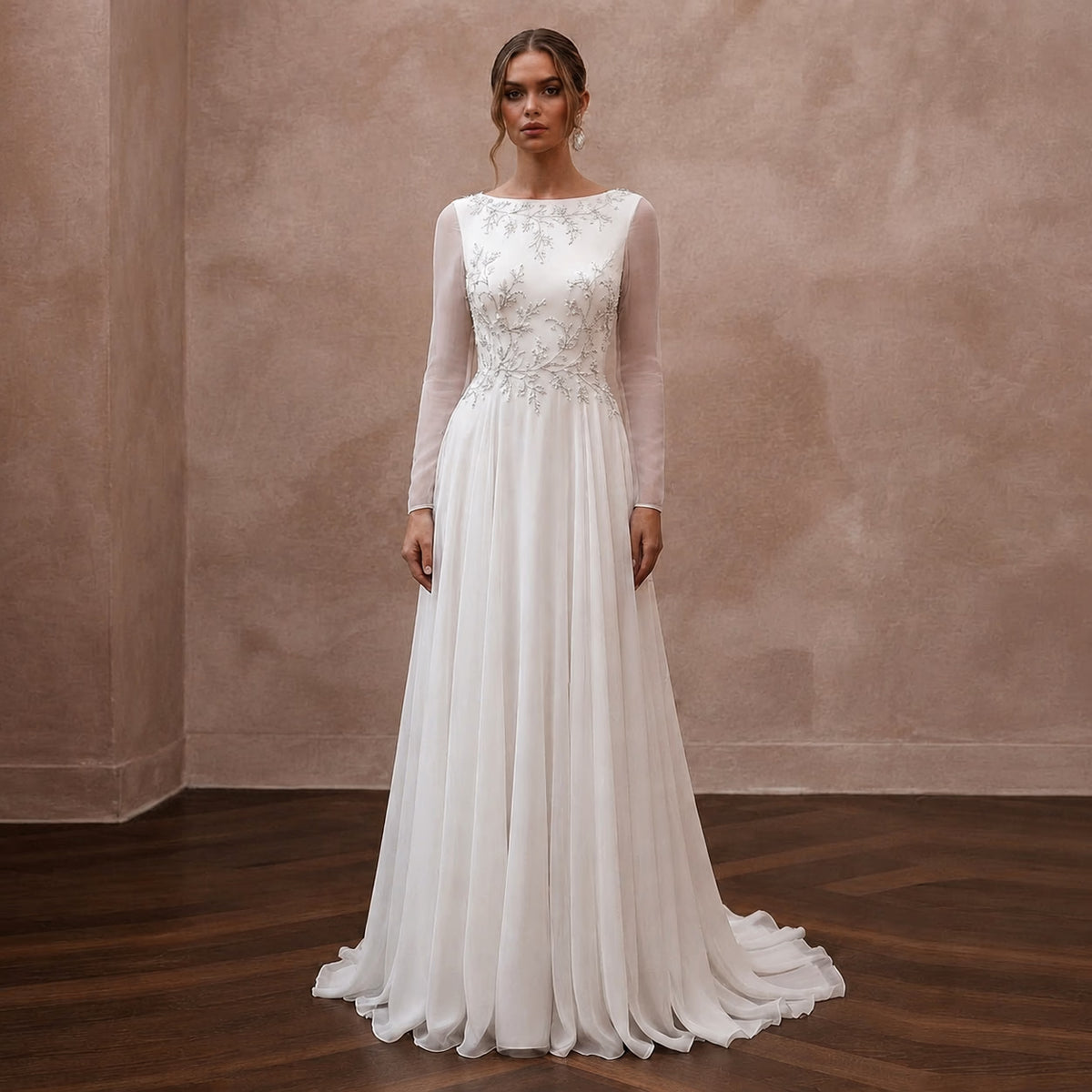 A woman stands in a studio wearing a long-sleeve white wedding gown with an embellished lace bodice and a flowing chiffon skirt, posed against a textured beige wall and dark wood floor. Main image