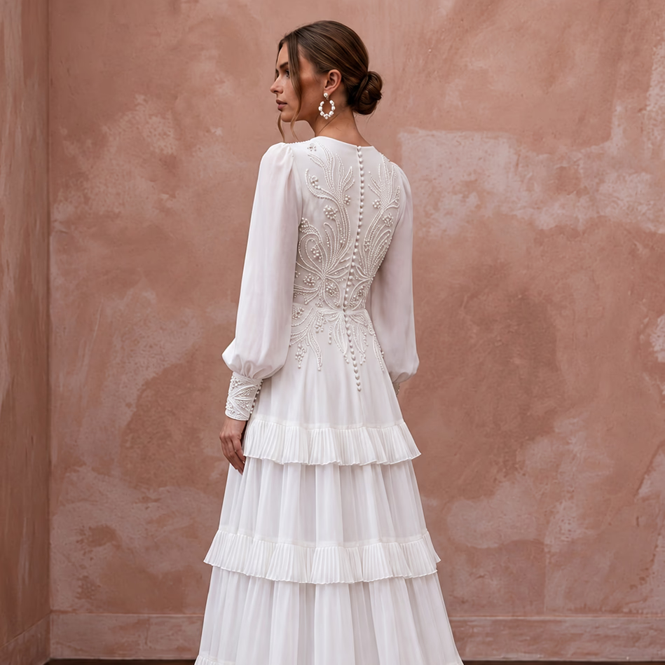 Elegant pure white chiffon gown featuring tiered skirt and long sleeves, adorned with intricate beadwork.