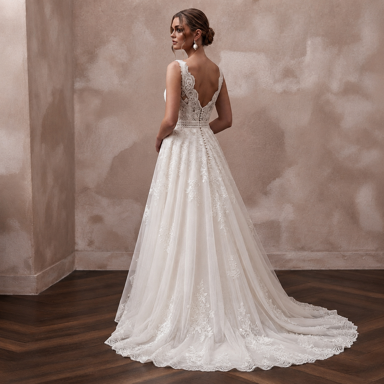 A woman wearing a white lace wedding gown stands with her back to the camera in an indoor setting with a textured beige wall and dark wood floor.